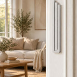 Extra Large Modern Silver Pyramid Mezuzah mounted vertically on a white interior doorpost, where its softly brushed silver aluminum mezuzah cover and three graduated bars create a minimalist Judaica accent with clean geometric lines against the pale doorframe