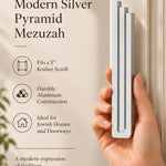 Hand holding the Extra Large Modern Silver Pyramid Mezuzah upright, revealing its softly brushed silver aluminum mezuzah cover, slender three-bar Pyramid design and graduated top beside illustrated product features for minimalist Jewish home Judaica