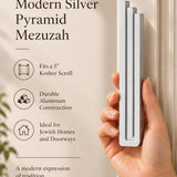 Hand holding the Extra Large Modern Silver Pyramid Mezuzah upright, revealing its softly brushed silver aluminum mezuzah cover, slender three-bar Pyramid design and graduated top beside illustrated product features for minimalist Jewish home Judaica