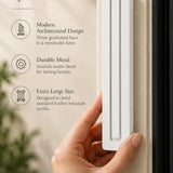 Extra Large Modern White Pyramid Mezuzah held beside a doorpost, with the smooth matte white aluminum mezuzah cover shown close enough to reveal its three stepped bars and rounded lower edge alongside product-name and design callouts for this contemporary Judaica piece
