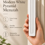 A hand presents the Extra Large Modern White Pyramid Mezuzah with its smooth matte white aluminum mezuzah cover facing forward, highlighting the clean graduated bars and geometric vertical profile beside design illustrations for a contemporary Jewish doorway accent