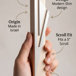 A hand holds a slim aluminum magnetic scroll protector with text callouts detailing its aluminum case, modern Shin design, Israeli origin, scroll fit, and included mounting tape against a neutral beige background.