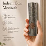 Female hand holding the exact vintage Judean coin mezuzah, demonstrating size and craftsmanship for a premium product feature display.