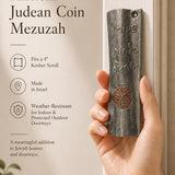 Female hand holding the exact vintage Judean coin mezuzah, demonstrating size and craftsmanship for a premium product feature display.
