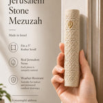 Female hand holding the Jerusalem stone mezuzah, highlighting its texture and gold details, in a warm natural light setting for store showcase.