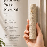 Female hand holding the Jerusalem stone mezuzah, highlighting its texture and gold details, in a warm natural light setting for store showcase.