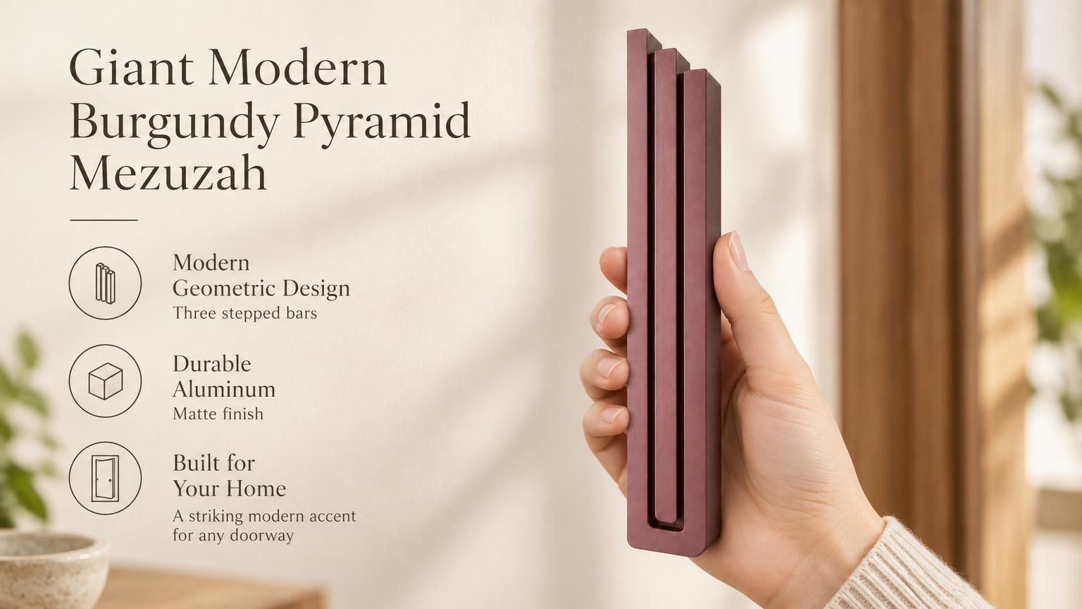 Giant Modern Burgundy Pyramid Mezuzah pictured in hand as a muted burgundy wine-red aluminum mezuzah cover with three graduated bars and a architectural stepped design, alongside its name and illustrated product features in a wide social-sharing image