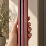 Hand holding the Giant Modern Burgundy Pyramid Mezuzah upright, showing the muted burgundy wine-red aluminum mezuzah cover with three graduated bars, a stepped top and rounded lower edge in a clear product view of its architectural design for a Jewish doorway