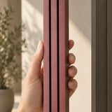 Hand holding the Giant Modern Burgundy Pyramid Mezuzah upright, showing the muted burgundy wine-red aluminum mezuzah cover with three graduated bars, a stepped top and rounded lower edge in a clear product view of its architectural design for a Jewish doorway