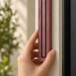 Giant Modern Burgundy Pyramid Mezuzah held against a pale doorpost, showing the muted burgundy wine-red aluminum mezuzah cover and its three ascending bars in close detail as a architectural Jewish doorway design with a clean stepped top and softly rounded base