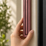 Giant Modern Burgundy Pyramid Mezuzah held against a pale doorpost, showing the muted burgundy wine-red aluminum mezuzah cover and its three ascending bars in close detail as a architectural Jewish doorway design with a clean stepped top and softly rounded base