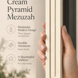 Hand holding the Giant Modern Cream Pyramid Mezuzah upright, revealing its warm ivory cream aluminum mezuzah cover, slender three-bar Pyramid design and graduated top beside illustrated product features for contemporary Jewish home Judaica