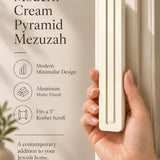 A hand presents the Giant Modern Cream Pyramid Mezuzah with its warm ivory cream aluminum mezuzah cover facing forward, highlighting the clean graduated bars and geometric vertical profile beside design illustrations for a contemporary Jewish doorway accent