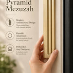 Giant Modern Gold Pyramid Mezuzah held beside a doorpost, with the warm metallic gold aluminum mezuzah cover shown close enough to reveal its three stepped bars and rounded lower edge alongside product-name and design callouts for this architectural Judaica piece