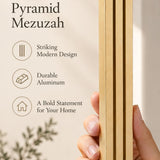 Hand holding the Giant Modern Gold Pyramid Mezuzah upright, revealing its warm metallic gold aluminum mezuzah cover, slender three-bar Pyramid design and graduated top beside illustrated product features for architectural Jewish home Judaica