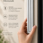 Giant Modern Silver Pyramid Mezuzah held beside a doorpost, with the softly brushed silver aluminum mezuzah cover shown close enough to reveal its three stepped bars and rounded lower edge alongside product-name and design callouts for this architectural Judaica piece