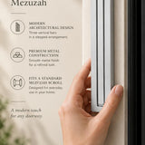 Giant Modern Silver Pyramid Mezuzah held beside a doorpost, with the softly brushed silver aluminum mezuzah cover shown close enough to reveal its three stepped bars and rounded lower edge alongside product-name and design callouts for this architectural Judaica piece