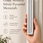 A hand presents the Giant Modern Silver Pyramid Mezuzah with its softly brushed silver aluminum mezuzah cover facing forward, highlighting the clean graduated bars and geometric vertical profile beside design illustrations for a architectural Jewish doorway accent