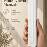 Hand holding the Giant Modern White Pyramid Mezuzah upright, revealing its smooth matte white aluminum mezuzah cover, slender three-bar Pyramid design and graduated top beside illustrated product features for architectural Jewish home Judaica