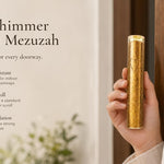 Gold Shimmer acrylic mezuzah case held beside a modern doorway, featuring a clear cylindrical acrylic body filled with sparkling gold accents and a subtle Hebrew Shin design. Made in Israel, this contemporary gold mezuzah case fits a 5-inch kosher mezuzah scroll and works beautifully on indoor or protected exterior doorways