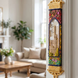Elegant golden Jerusalem Garden mezuzah mounted on a doorframe, showcasing its ornate gold trim, colorful floral details, and Jerusalem scene, in a home interior.