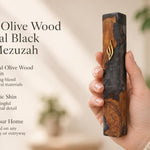 Person holding a handcrafted olive wood and black resin mezuzah featuring a gold Shin letter in a warm, naturally lit setting.