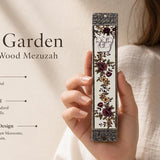 Person holding the Heritage Rose Garden Mezuzah made from wood and metal, highlighting floral design and Hebrew letter