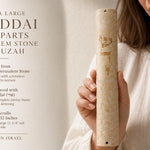 Premium hand-held view of the Jerusalem stone Shaddai Ramparts Mezuzah showing Hebrew engravings and textured surface, balanced with editorial text.