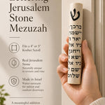 Close-up of person holding Jerusalem Stone Mezuzah, showing detailed black Hebrew lettering and cylindrical shape, on a natural background.