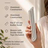 Person holding the exact silver mezuzah with natural lighting and generous negative space around.