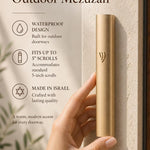 Close-up of a person holding the gold aluminum outdoor mezuzah, with editorial text space on the side, highlighting its elegant simplicity and protective finish.