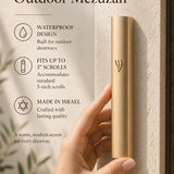 Close-up of a person holding the gold aluminum outdoor mezuzah, with editorial text space on the side, highlighting its elegant simplicity and protective finish.