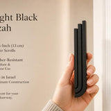 Person holding modern black aluminum mezuzah with three ascending rectangular bars, showing scale and design for door mounting.
