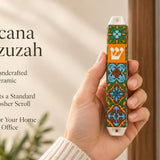Close-up of a person holding the artisanal ceramic Toscana Mezuzah decorated with orange, deep green, and pale blue tile patterns.
