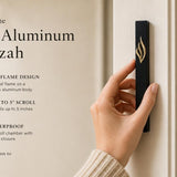 Person holding the exact black aluminum mezuzah with gold flame emblem, displaying its design and dimensions for ceremonial use.