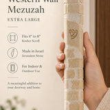Hand holding the Kotel extra large cream stone mezuzah, showing the carved stone courses and texture.