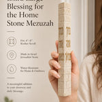 Hand holding the Birkat HaBayit cream Jerusalem stone mezuzah showing the gold home blessing lettering.