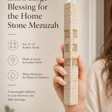 Hand holding the Birkat HaBayit cream Jerusalem stone mezuzah showing the gold home blessing lettering.