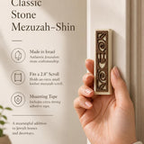 Close-up of a person holding a Jerusalem stone mezuzah, showcasing texture, shape, and size, in a soft natural light setting for store display.