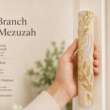 Person holding a large Jerusalem stone mezuzah with gold olive branch and Hebrew Shin in a key demonstration of size and craftsmanship.