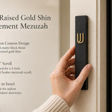 A person holding a Timeless black cement mezuzah case made in Israel with a raised gold Shin, narrow six-inch profile, and clean contemporary design mounted on a doorway