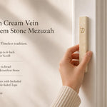 Person holding the classic golden cream vein Jerusalem stone mezuzah case in natural warm lighting mounted to the doorway with product feature callouts