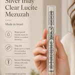 A person holding a clear lucite mezuzah with a floating silver inlay in a premium editorial style.