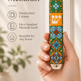 Hand holding the Toscana ceramic mezuzah case featuring intricate geometric patterns and a central Hebrew letter Shin.