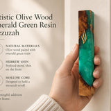 Person holding an artistic olive wood and emerald green resin mezuzah case with a gold-toned Shin letter for a Jewish home.