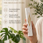 Person holding a textured white concrete mezuzah featuring a golden Shin symbol in a bright minimalist setting.