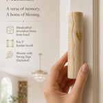 A person holding a handcrafted Jerusalem stone wedding mezuzah case with gold accents in a soft-lit editorial setting.