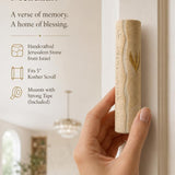 A person holding a handcrafted Jerusalem stone wedding mezuzah case with gold accents in a soft-lit editorial setting.