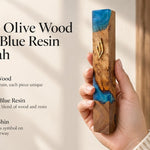 Close-up of a person holding an olive wood and turquoise resin mezuzah featuring a traditional gold Hebrew Shin symbol.