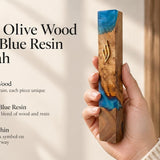 Close-up of a person holding an olive wood and turquoise resin mezuzah featuring a traditional gold Hebrew Shin symbol.
